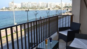 A balcony with wicker furniture, a glass table, and a view of the sea and buildings. - Le Malte House St Julians (St. Julian's)