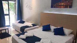 A hotel room with two beds, each with a blue pillow and white bedding. There is a small table and a wall with a 'Welcome' sign. - Le Malte House St Julians (St. Julian's)