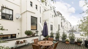A rooftop terrace with a round wooden table and chairs, surrounded by potted plants and a satellite dish. - Cleveland Square Mansions (London)