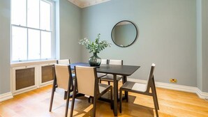 A dining room with a dark wooden table, four chairs, a vase with flowers, and a round mirror on the wall. - Cleveland Square Mansions (London)