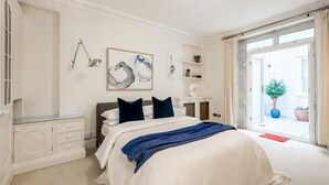 A bedroom with a bed, bedside tables, a lamp, a painting, and a view of the outside. - Cleveland Square Mansions (London)