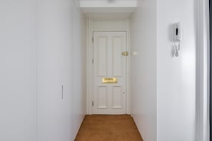 A narrow hallway with a white door and a wall-mounted phone.