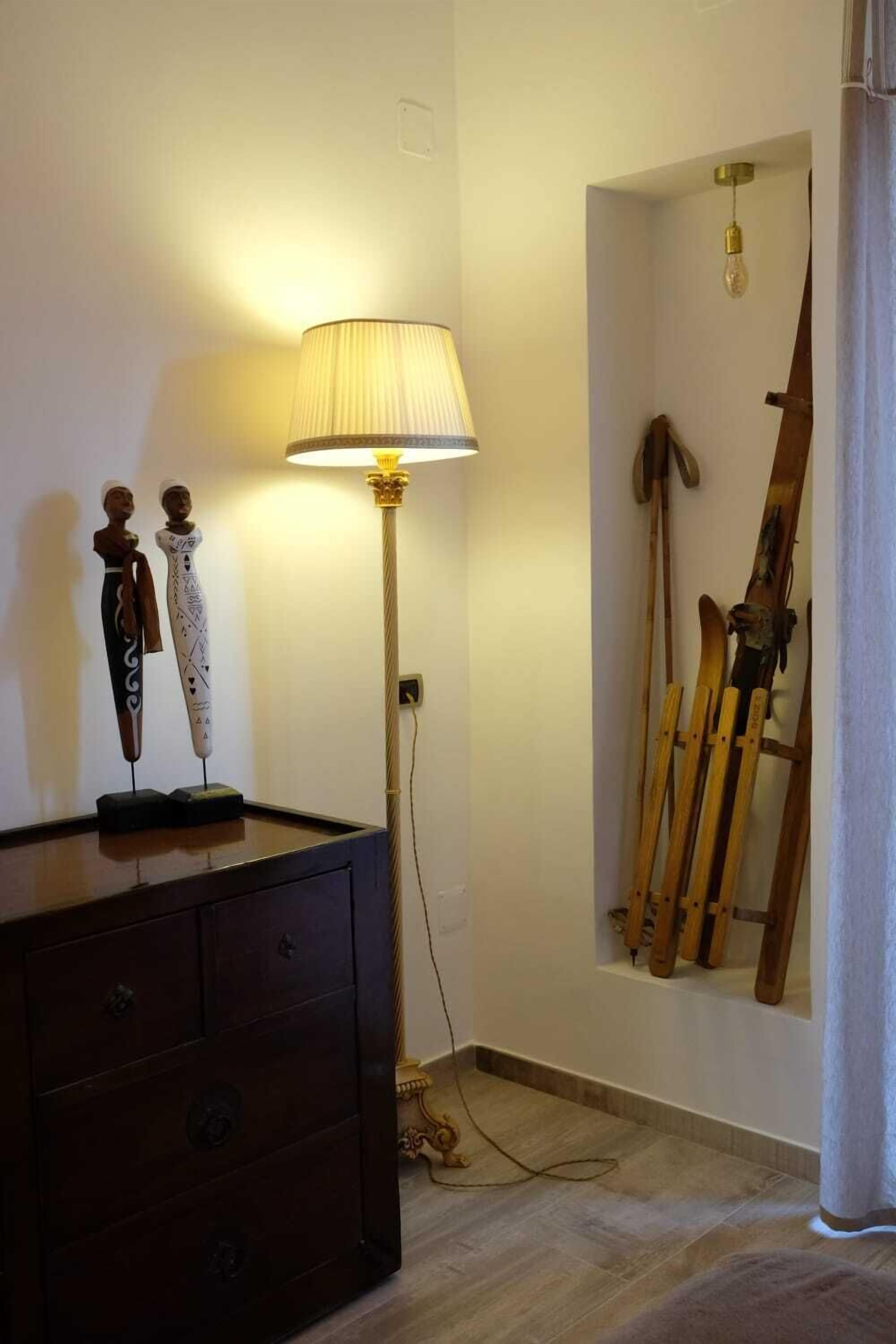 Een kamer met een houten dressoir, een staande lamp en ski's die tegen de muur leunen.