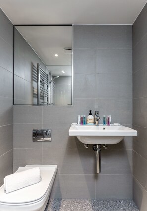 A modern bathroom with a white sink, grey tiles, and a towel on the floor.