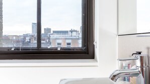 A bathroom with a large window, a white sink, and a mirror. - Greek Street Penthouse (London)