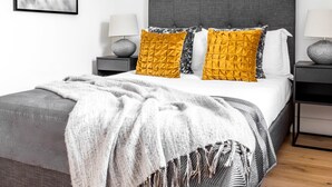 A modern bedroom with a grey upholstered bed, a white and grey patterned throw blanket, and two bedside tables with lamps. - Greek Street Penthouse (London)