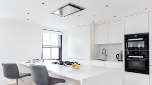 A modern kitchen with a central island, two bar stools, a built-in oven, and a window. - Greek Street Penthouse (London)