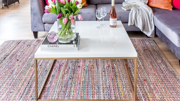 A modern living room with a grey sofa, colorful pillows, a white coffee table, and a vase of flowers. - Greek Street Penthouse (London)
