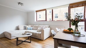 A modern living room with a sofa, a coffee table, and a dining table with fruit and flowers. - Richardsons Mews by Lime Street (London)