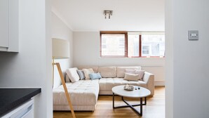 A modern living room with a sectional sofa, a round coffee table, and a lamp. - Richardsons Mews by Lime Street (London)
