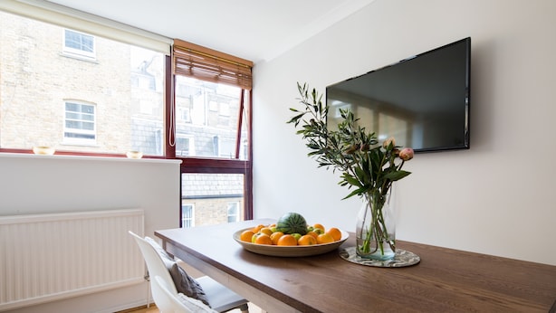 A dining area with a wooden table, a bowl of fruit, and a vase of flowers. - Richardsons Mews by Lime Street (London)
