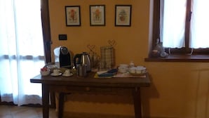 A dining table with various kitchen items, a coffee maker, and a window with curtains. - Cascina Marie (Bricherasio)