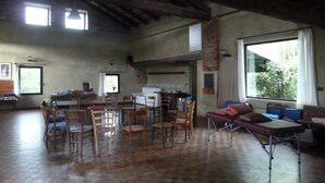 A spacious room with a high ceiling, wooden beams, a large window, and a mix of seating including chairs and a sofa. - Cascina Marie (Bricherasio)
