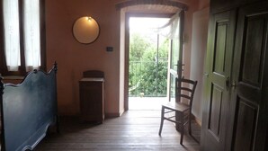 A room with a wooden floor, a blue chair, a wooden cabinet, and a window with curtains. - Cascina Marie (Bricherasio)