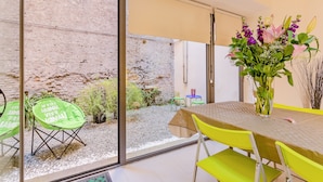 A dining area with a table and chairs, a vase with flowers, and a view through a glass door to an outdoor space with plants and a brick wall. - Rome as you feel - Selci Apartment (Rome)