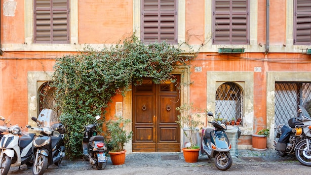 A building with a wooden door, potted plants, and parked scooters. - Rome as you feel - Selci Apartment (Rome)