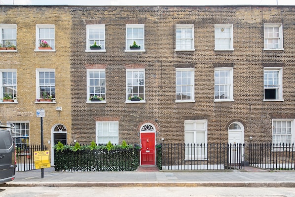 A row of brick townhouses with white-framed windows, a red door, and a black metal fence.