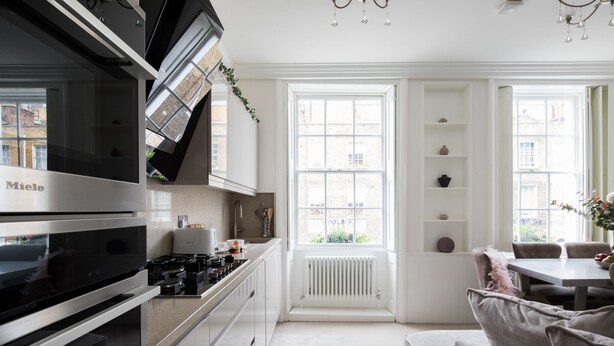 A modern kitchen with a built-in stove, white cabinetry, and a dining area with a table and chairs. - Star Street by Lime Street (London)