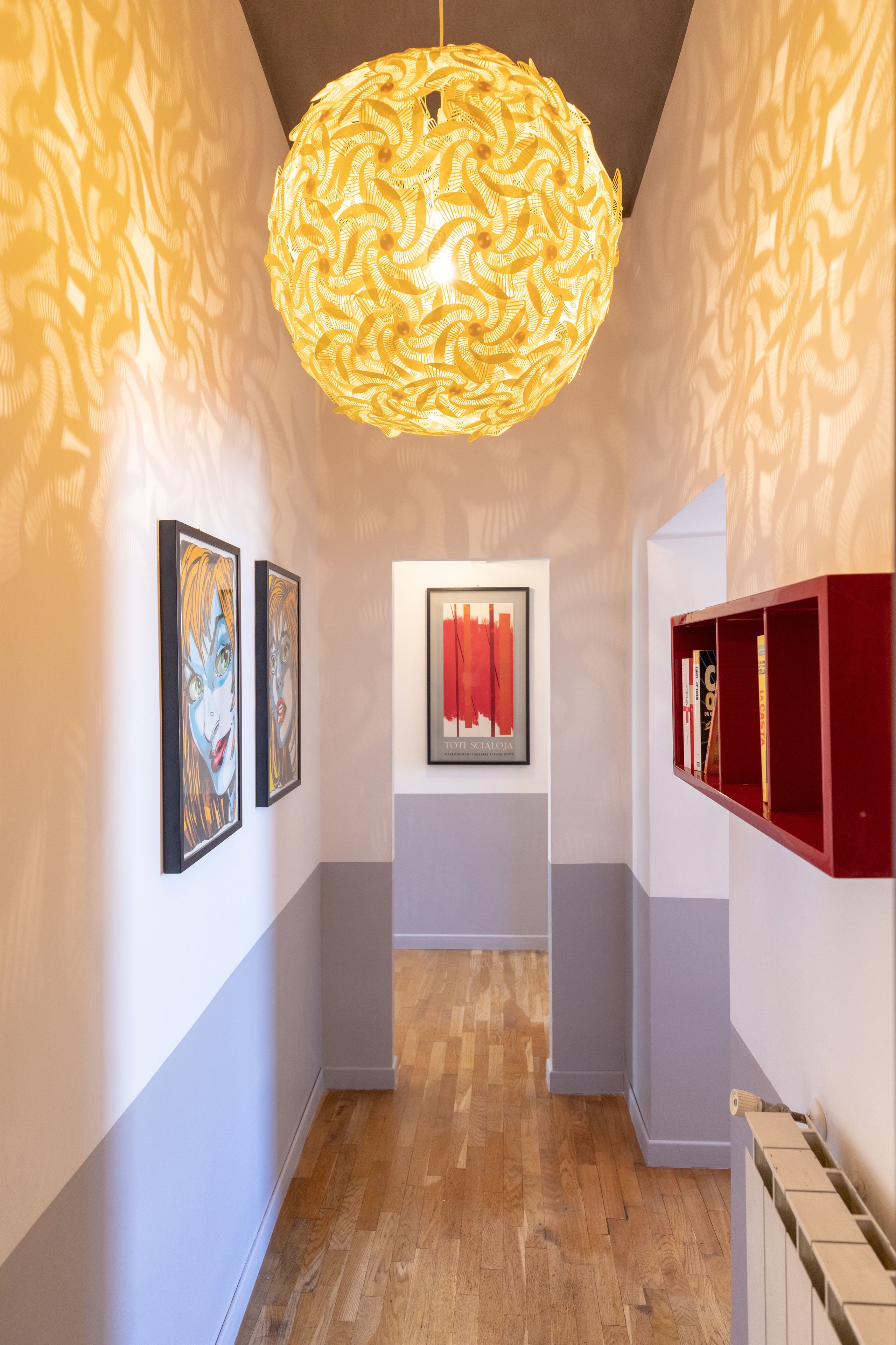 Un couloir aux murs ornés de motifs, doté d’un plancher en bois et d’un luminaire suspendu.