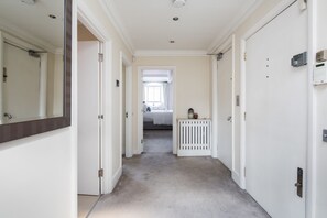 A narrow hallway with white walls and a carpeted floor leading to a bedroom. - Park Street Mayfair (London)