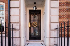 A black metal door with a gold emblem, flanked by white columns and a brick wall. - Park Street Mayfair (London)
