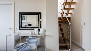 Ein modernes Schlafzimmer mit Glastisch, großem Spiegel, Holztreppe und weißer Tür.