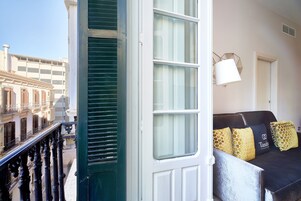 Un balcón con vista a un edificio, una puerta blanca y un sofá negro con cojines estampados.