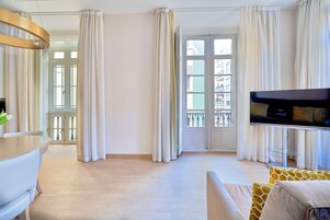 A modern living room with a flat-screen TV, a sofa, and a dining area with a table and chairs.