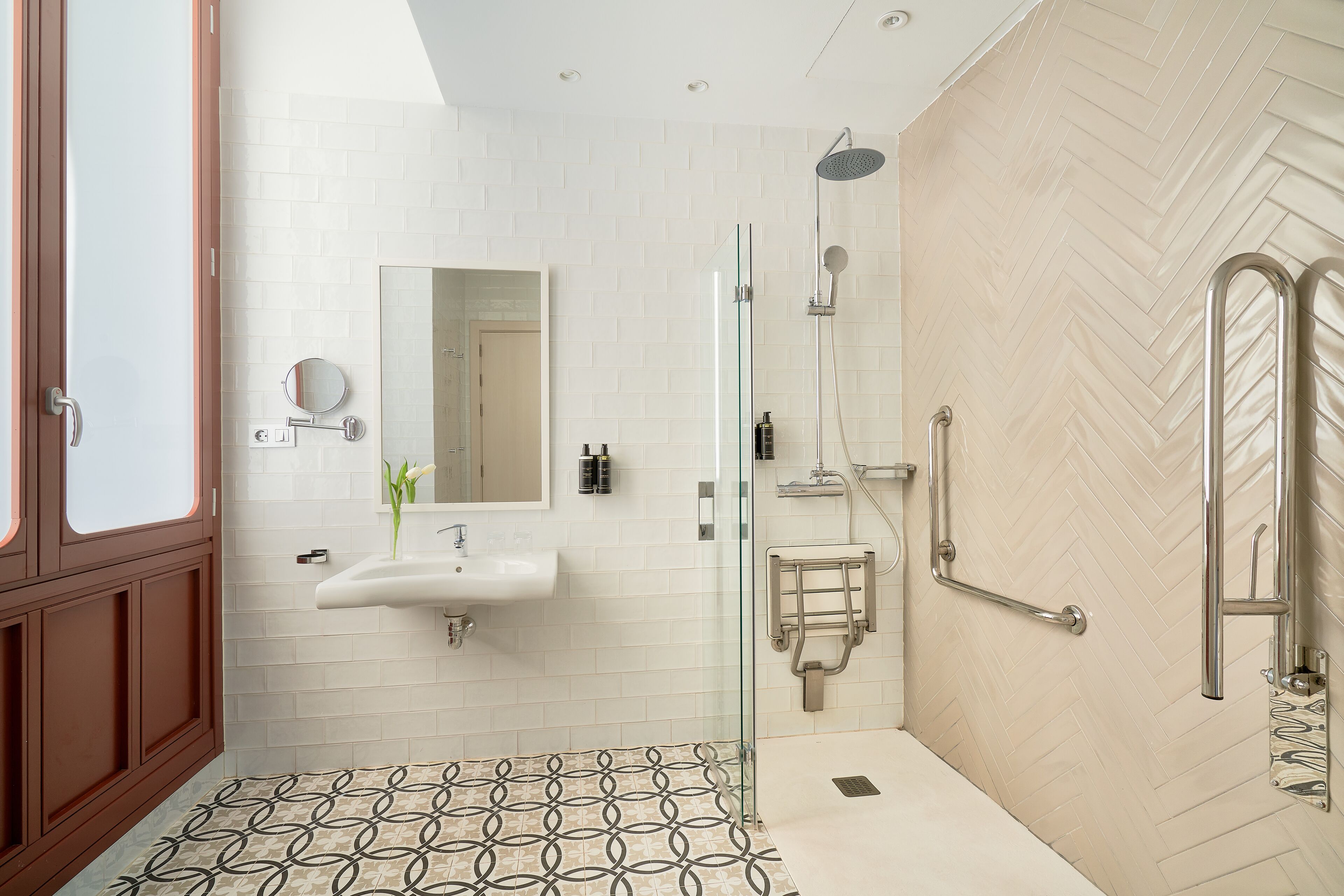 A modern bathroom with a glass-enclosed shower, a sink with a mirror, and a patterned floor.