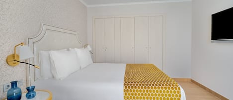 A hotel room with a bed, a bedside table with two vases, a wall-mounted TV, and a wardrobe.