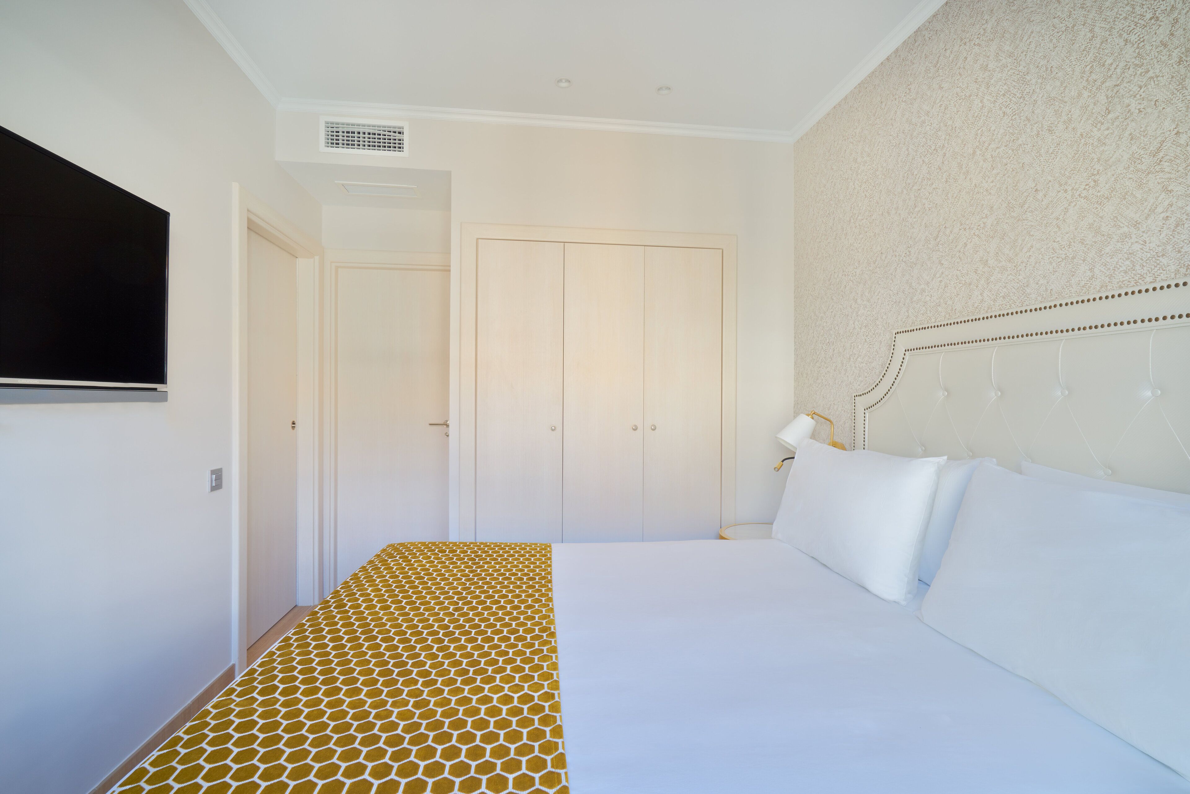 Een slaapkamer met een bed, een aan de muur bevestigde televisie en een deur naar een andere kamer.