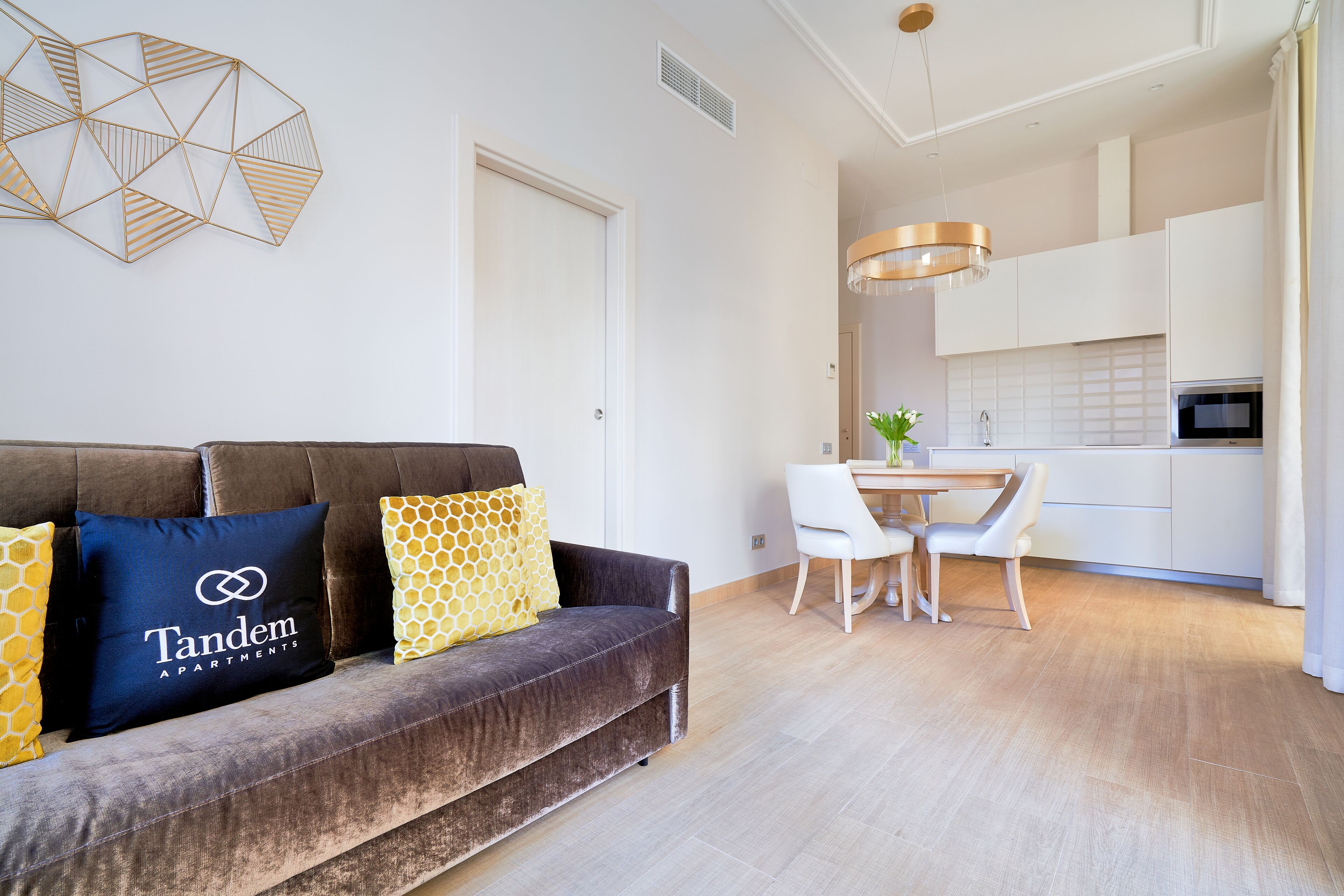 Un salon moderne avec un canapé marron foncé, une table à manger avec des chaises et un coin cuisine doté de meubles blancs et d’un four à micro-ondes.