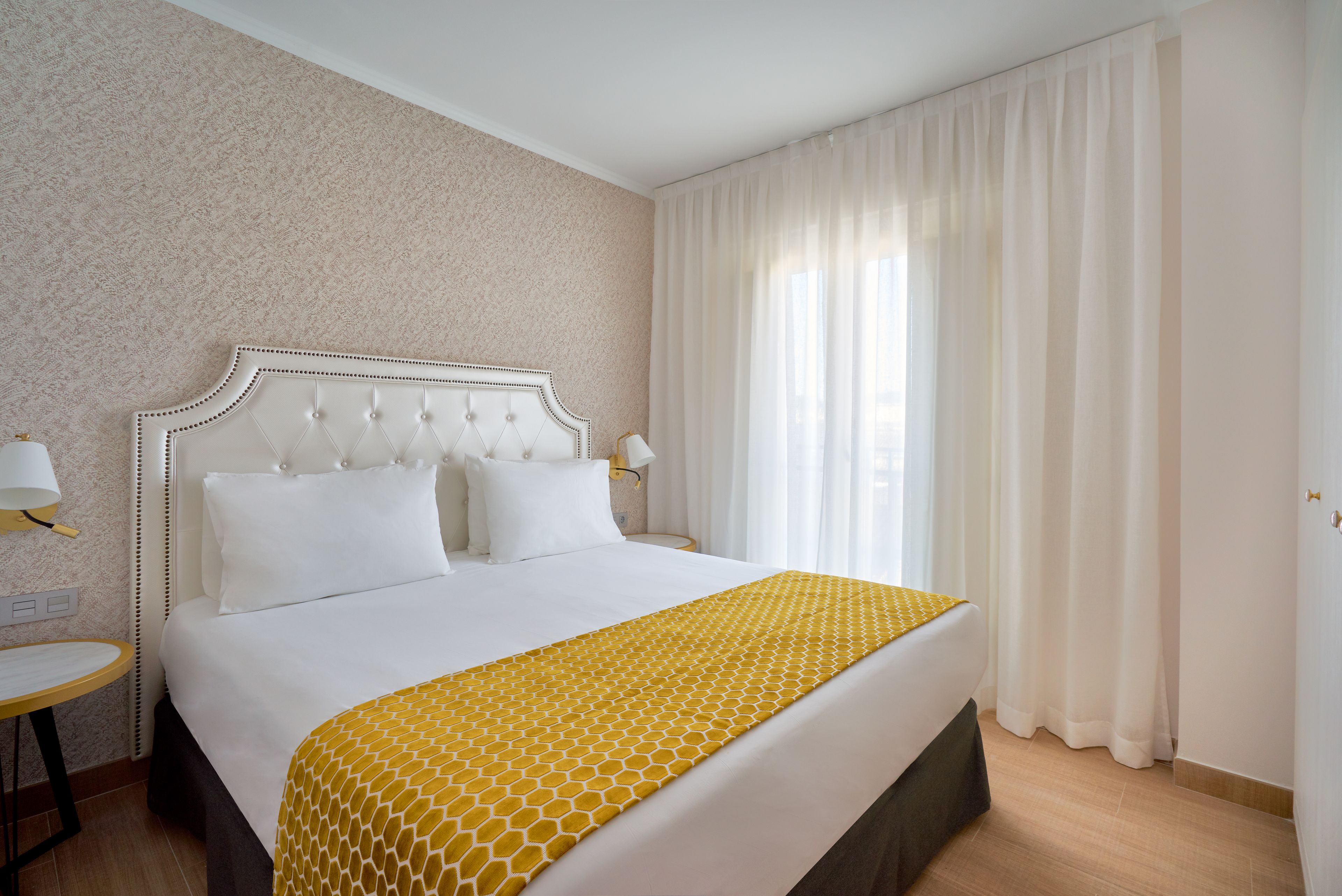 Una habitación de hotel con una cama grande, una mesita de noche y una ventana con cortinas.