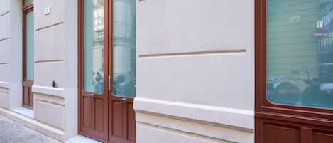 A building facade with a large brown door, a window with a reflection, and a small sign above the door.