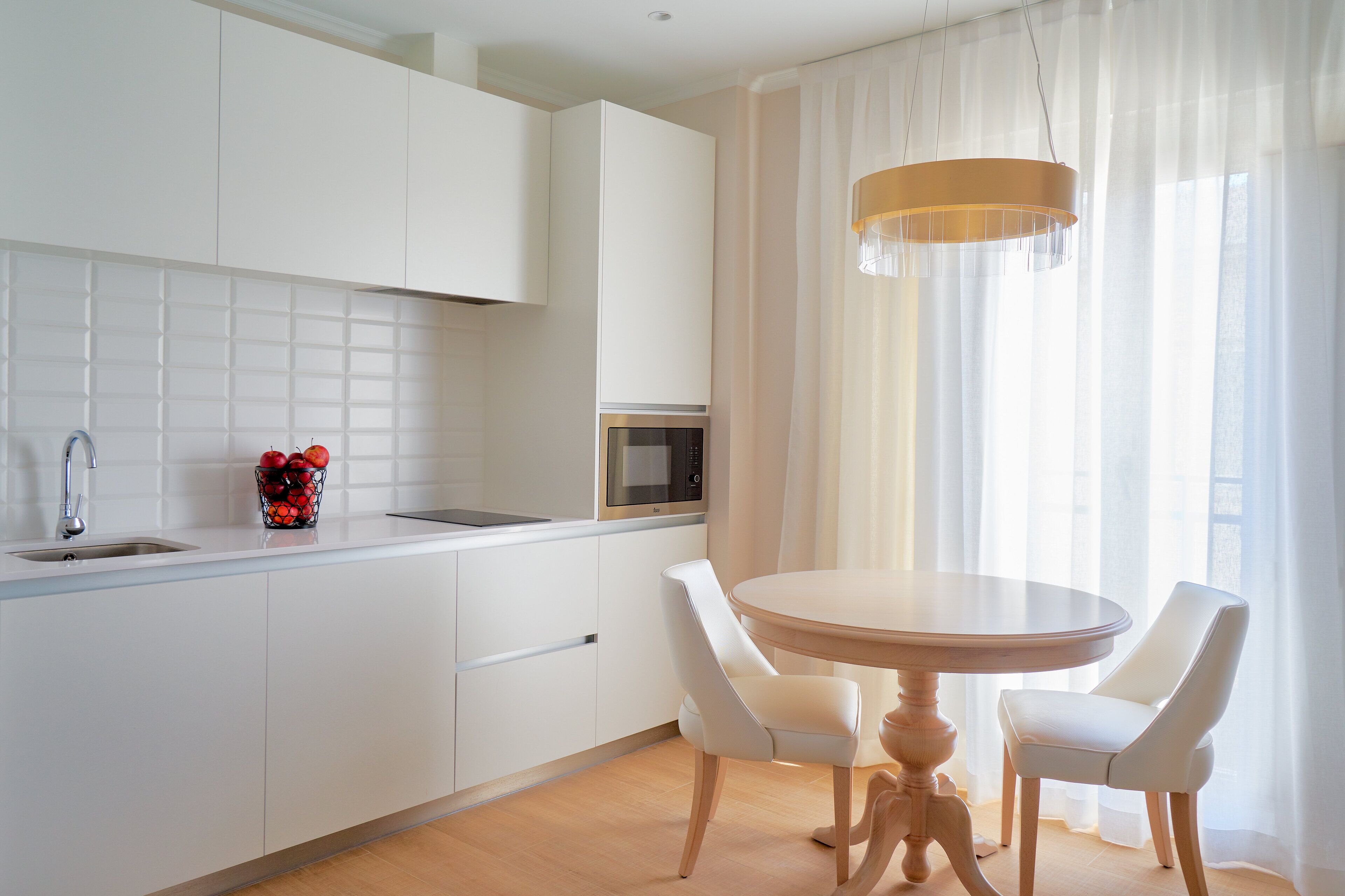 Una cocina moderna con armarios blancos, microondas integrado y una mesa de comedor redonda con dos sillas blancas.