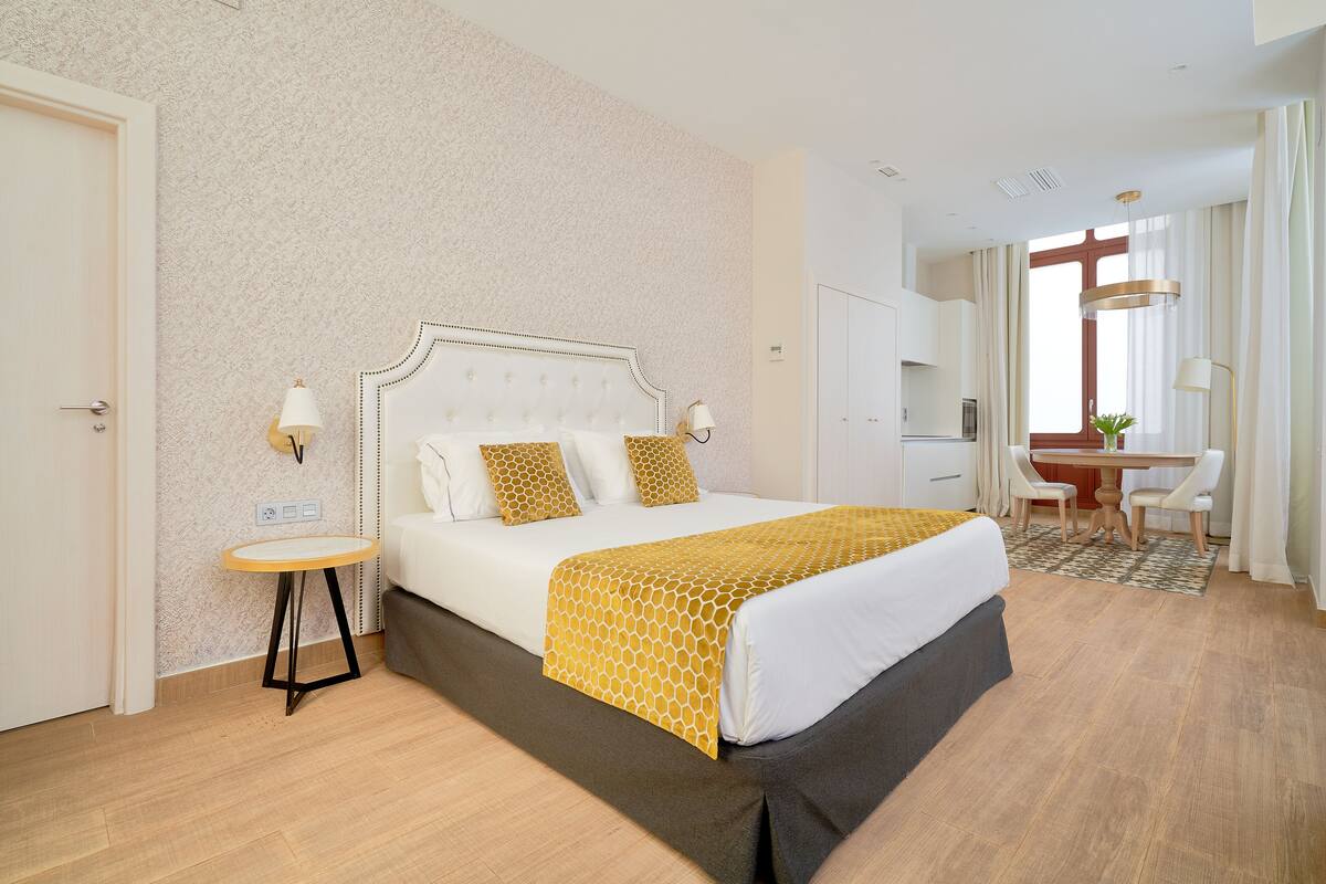 Una habitación de hotel con cama, mesita de noche, lámpara y escritorio con sillas.