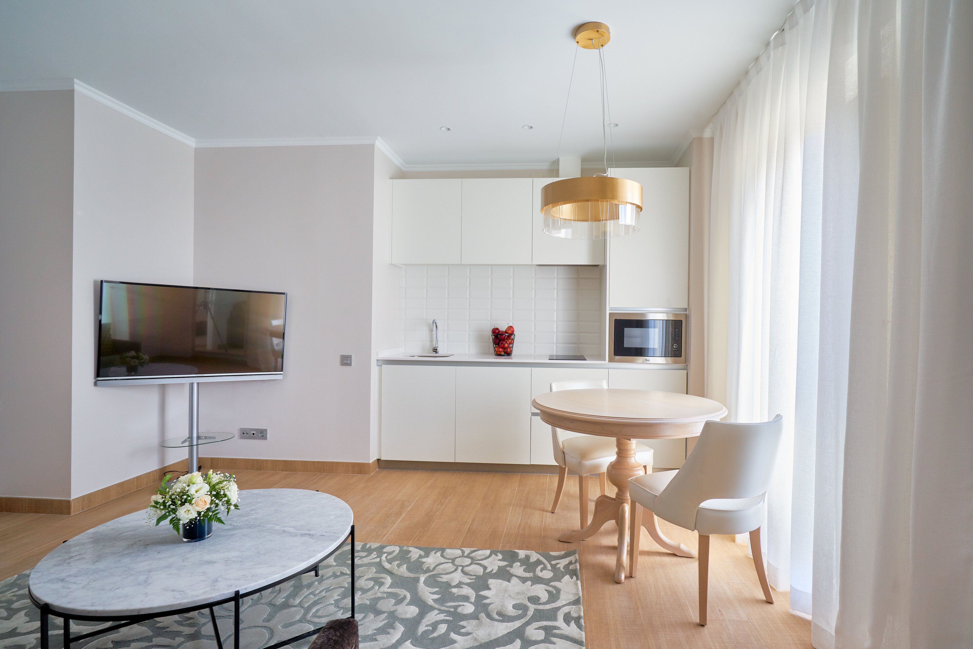 A modern kitchen with white cabinets, a round dining table, and a TV mounted on the wall.