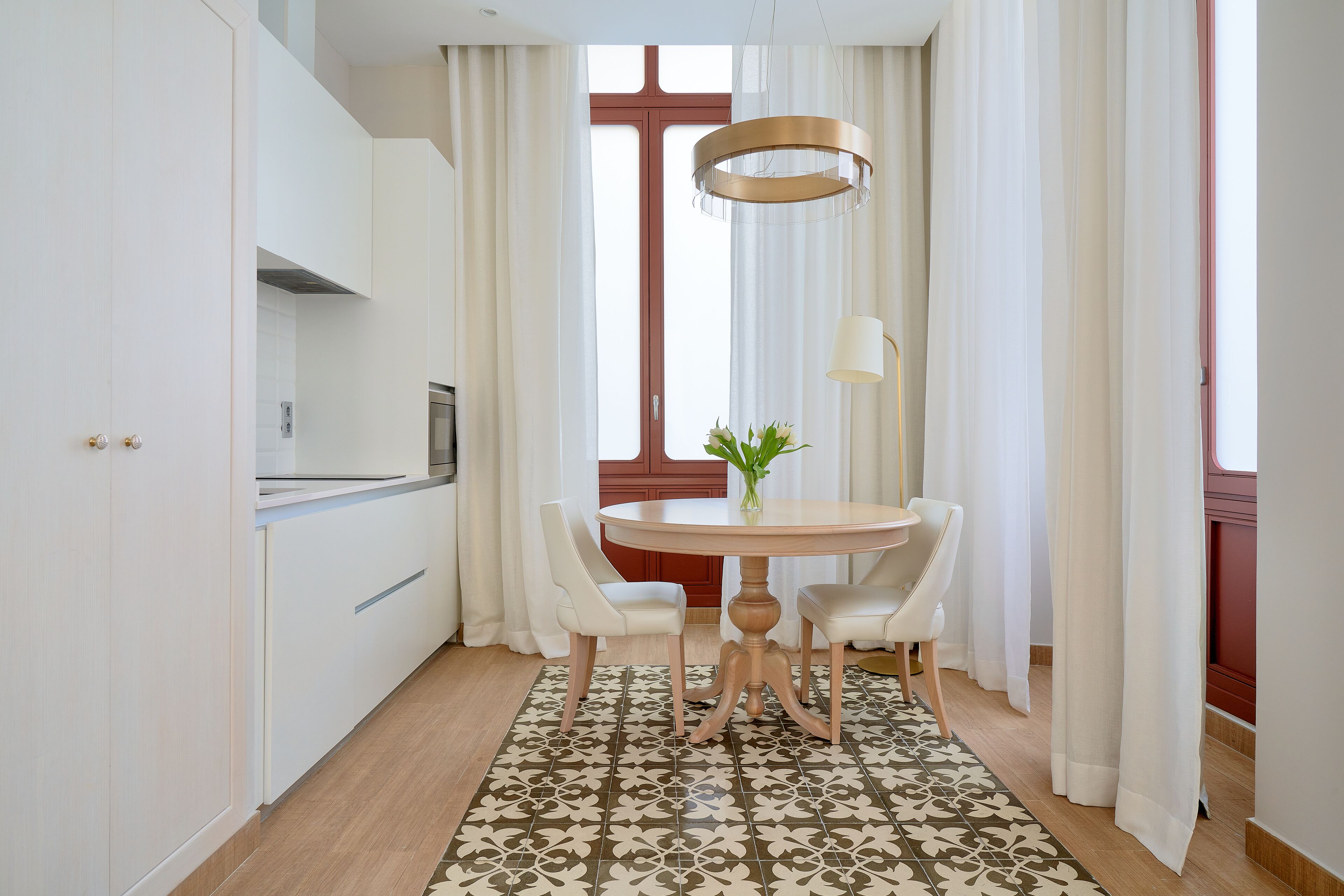 A modern kitchen with white cabinetry, a round dining table with two chairs, and a patterned rug.