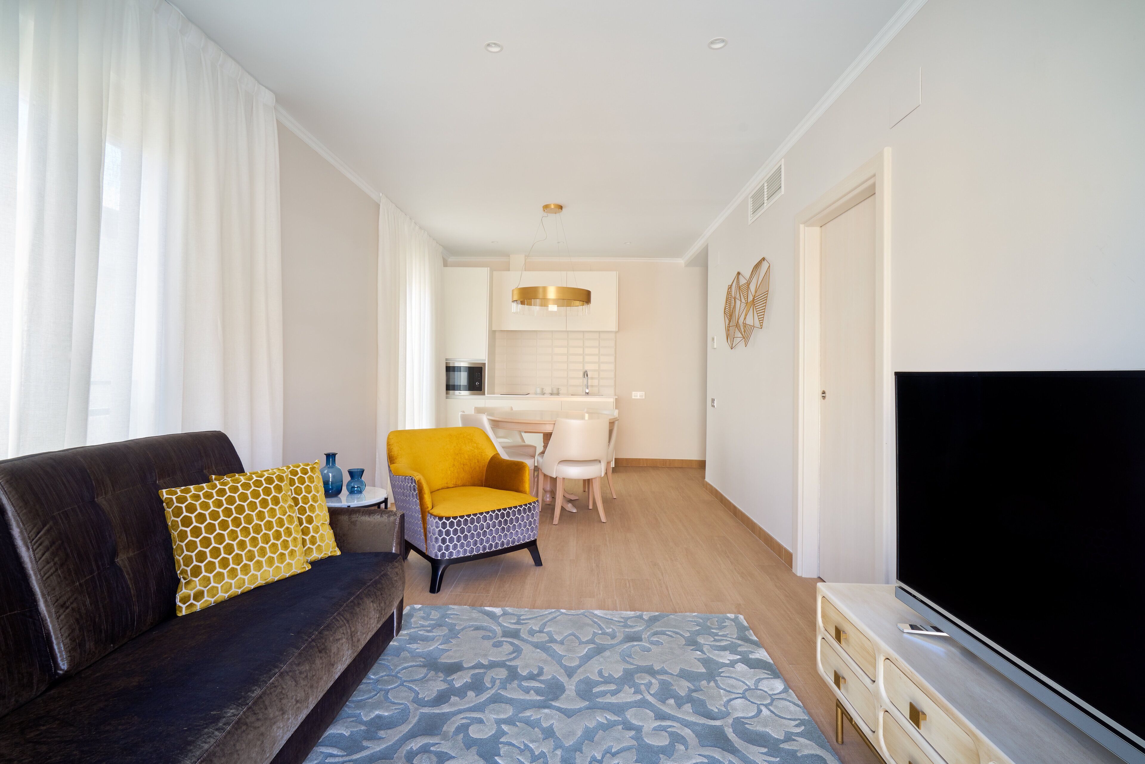 Een moderne woonkamer met een donkere bank, een vloerkleed met een patroon, een gele fauteuil en een flatscreen-televisie.