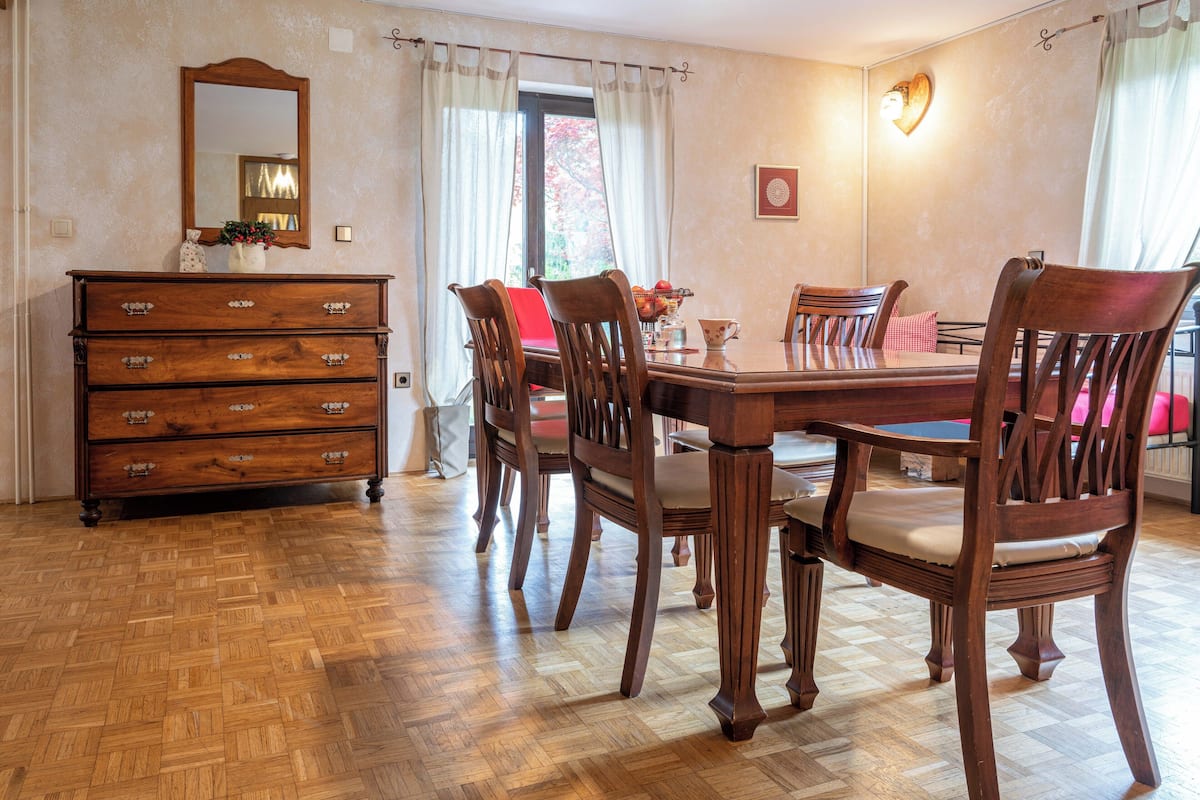 Ein Essbereich mit Holztisch und -stühlen, einer Holzkommode und einem Spiegel an der Wand.