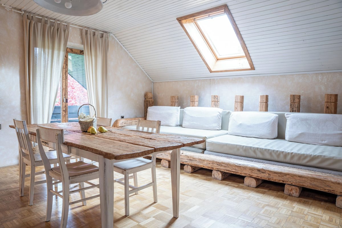 Ein gemütliches Schlafzimmer im Loft-Stil mit Esstisch aus Holz, weißem Sofa und einem Oberlicht.