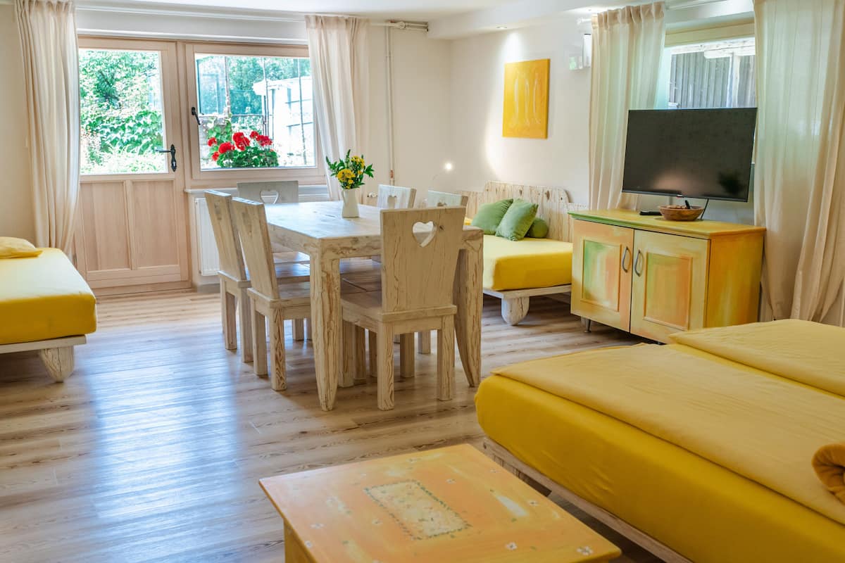 Ein Zimmer mit Holztisch, gelben Sofas, einem Fernseher und einem Fenster mit Vorhängen.