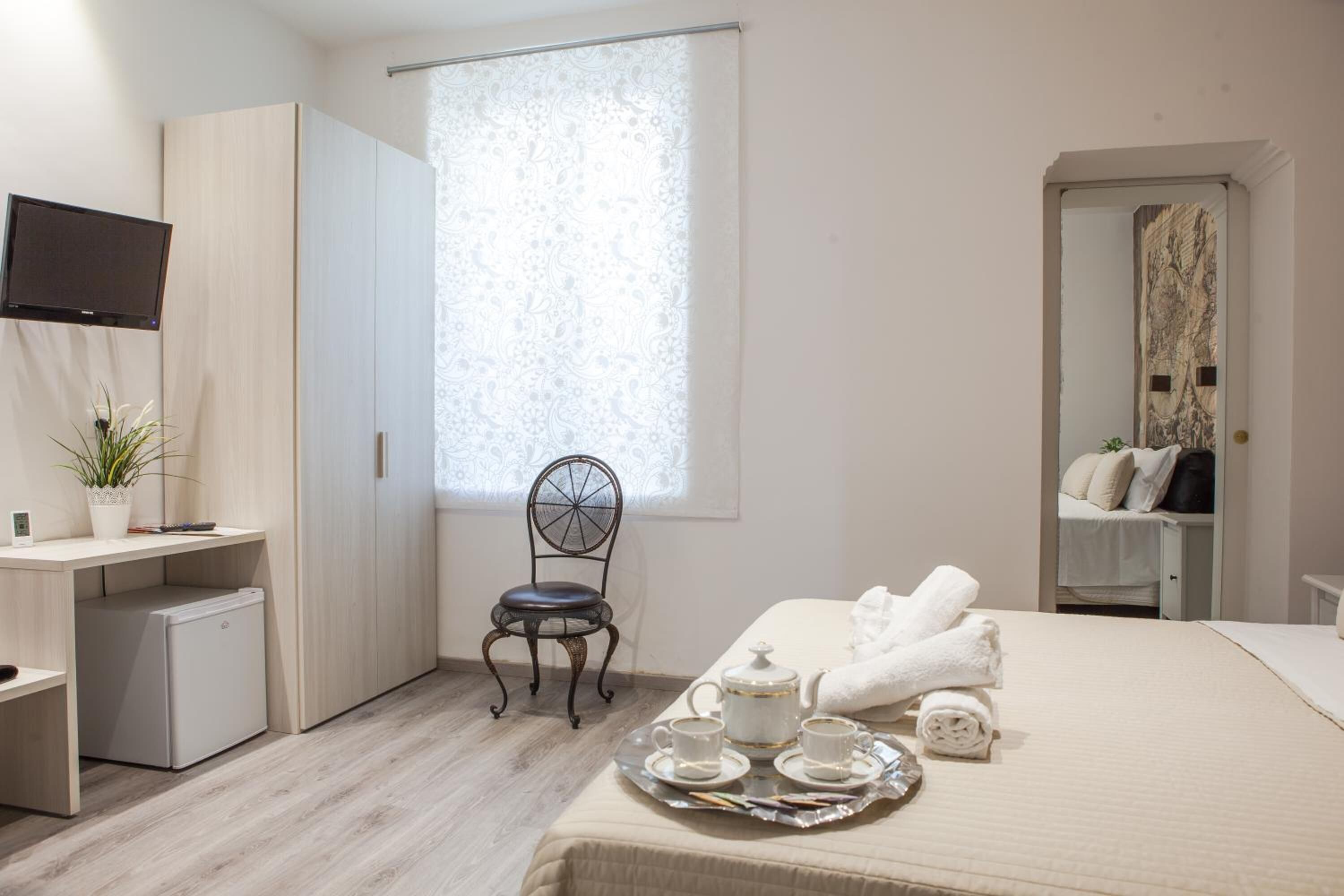 A hotel room with a bed, a desk, a chair, a TV, and a window with curtains.