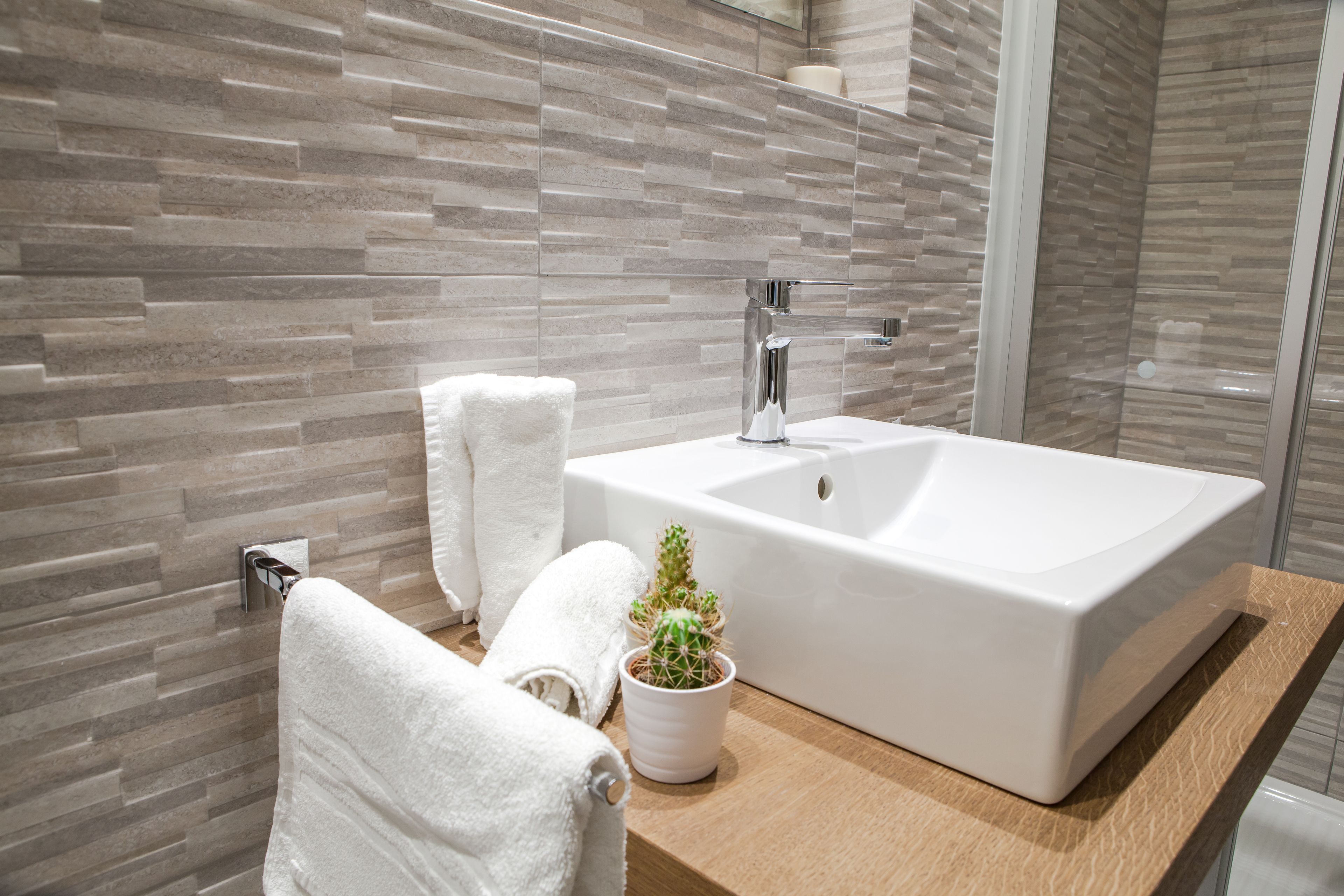 Ein Badezimmer mit einem rechteckigen Waschbecken, einem weißen Handtuch und einem Topf mit einem Kaktus.