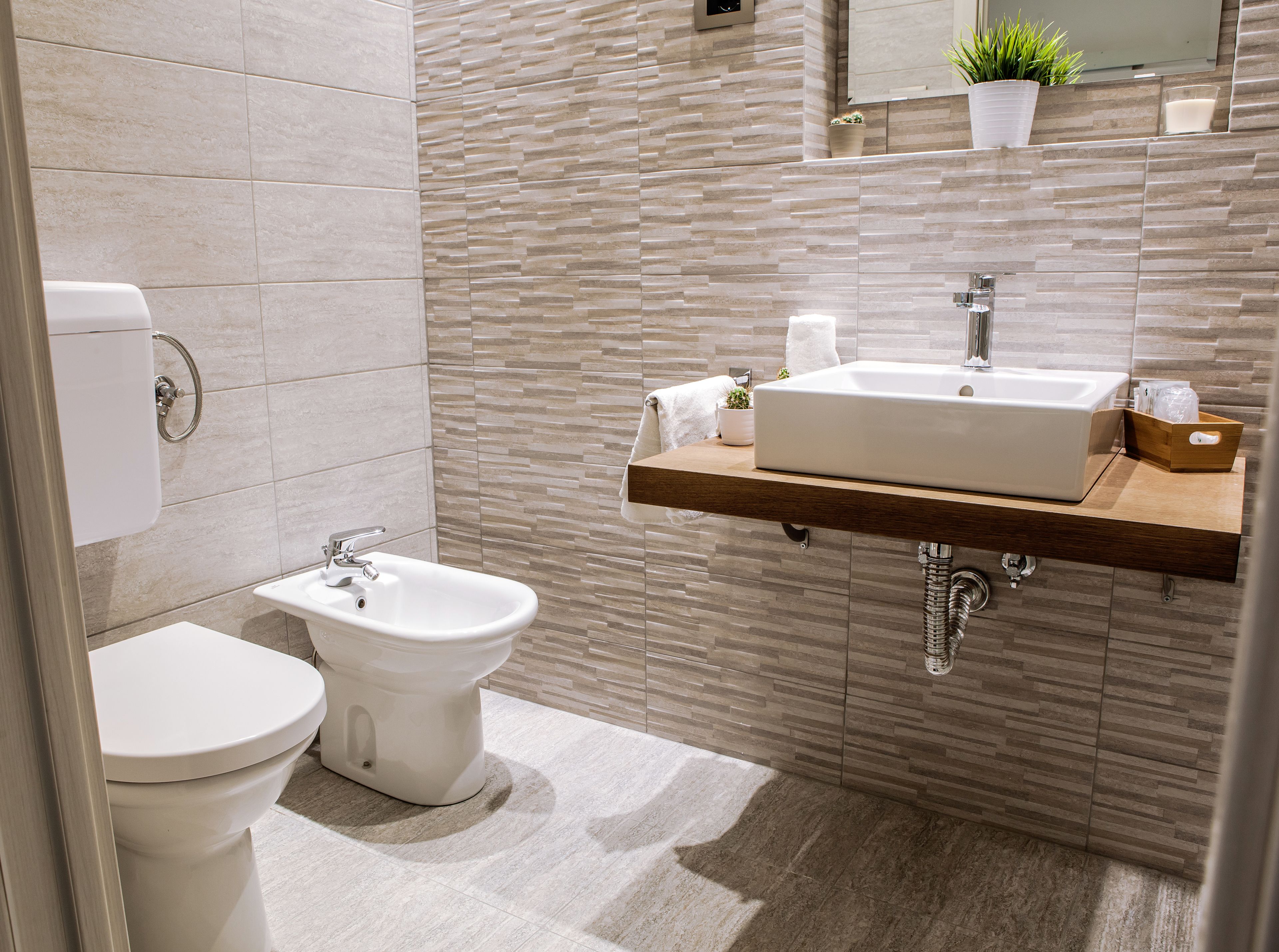 Een moderne badkamer met toilet, bidet en een wastafel met houten blad.