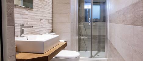 Un baño moderno con cabina de ducha de vidrio, tocador de madera y inodoro blanco.