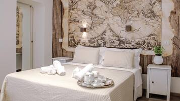 Habitación de hotel con un gran mapa antiguo en la pared, una cama bien hecha con ropa blanca y una bandeja con tazas de té y una tetera.