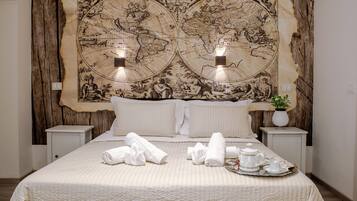 Une chambre d’hôtel avec une grande fresque représentant une carte géographique au mur, un lit bien fait avec des serviettes, et un plateau avec une théière et des tasses.