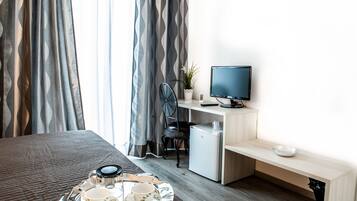 Habitación de hotel con cama, escritorio con computadora, refrigerador pequeño y bandeja con tazas y platillos.