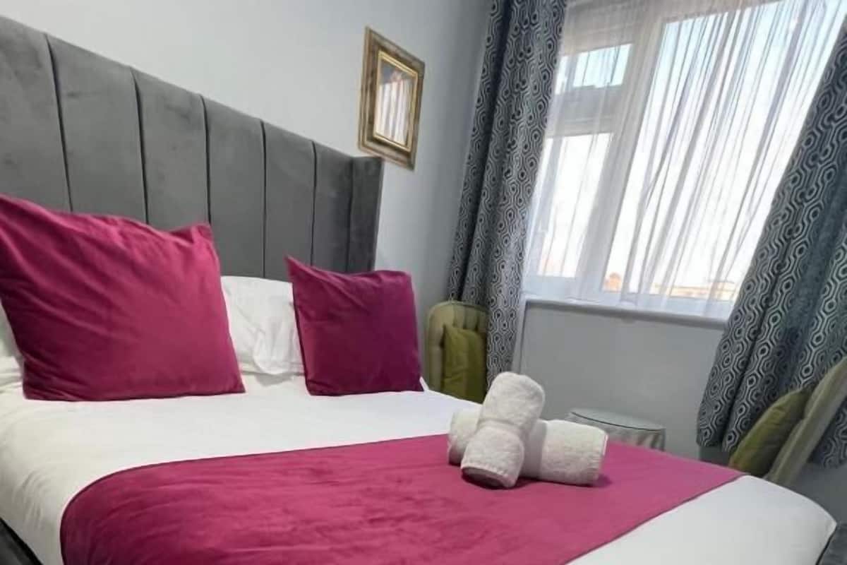 A bed with a grey headboard, white and pink bedding, and a red throw blanket.